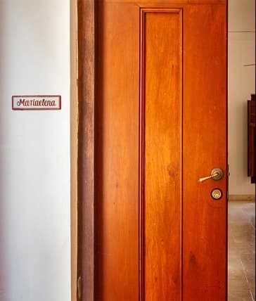 Una puerta de madera lisa y barnizada con manija metálica, ubicada junto a una pared blanca que tiene un pequeño letrero enmarcado.